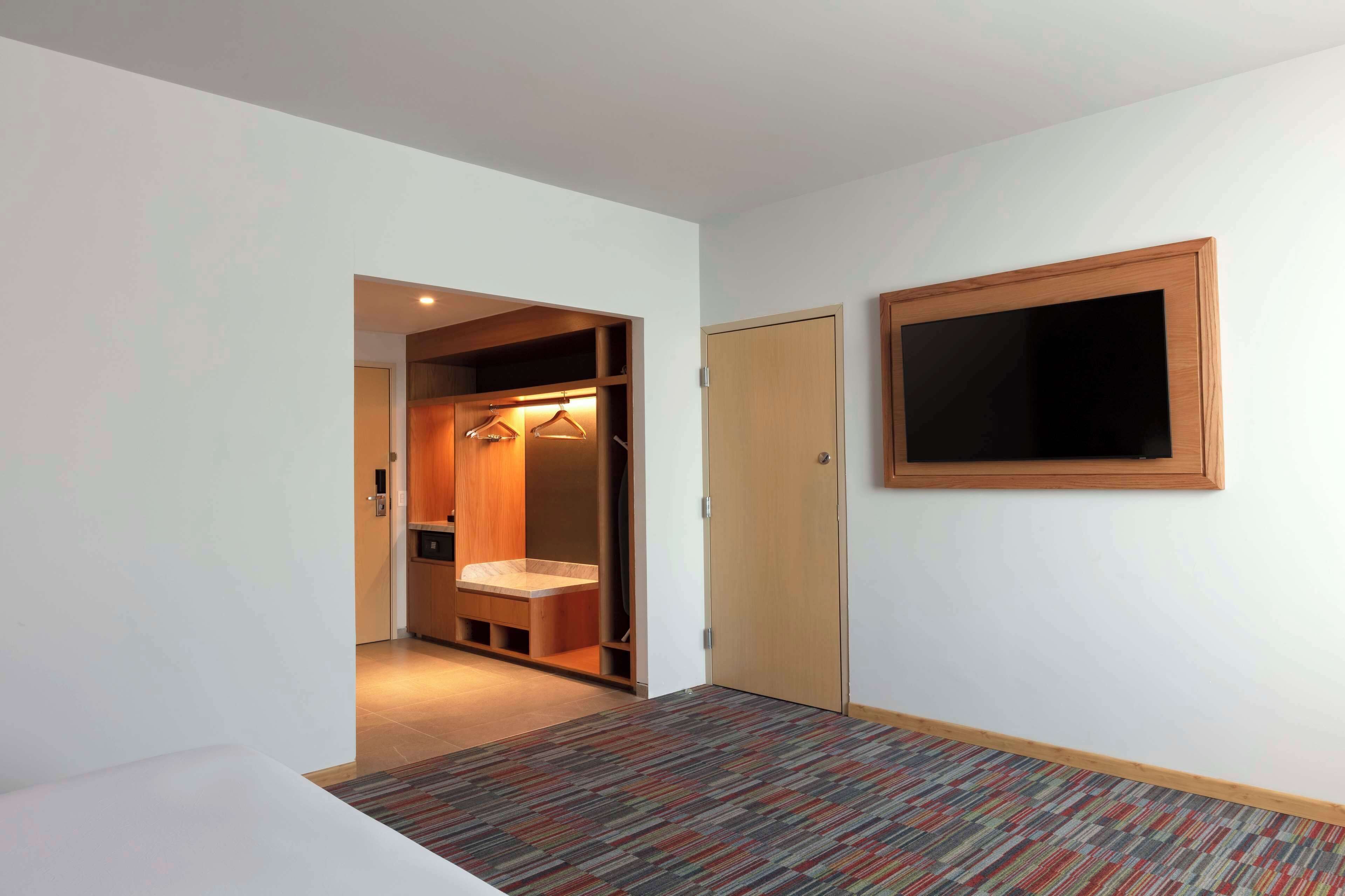 A hotel room with a walk-in closet, a wooden door, and a mounted TV.