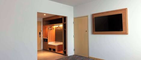 A hotel room with a walk-in closet, a wooden door, and a mounted TV.
