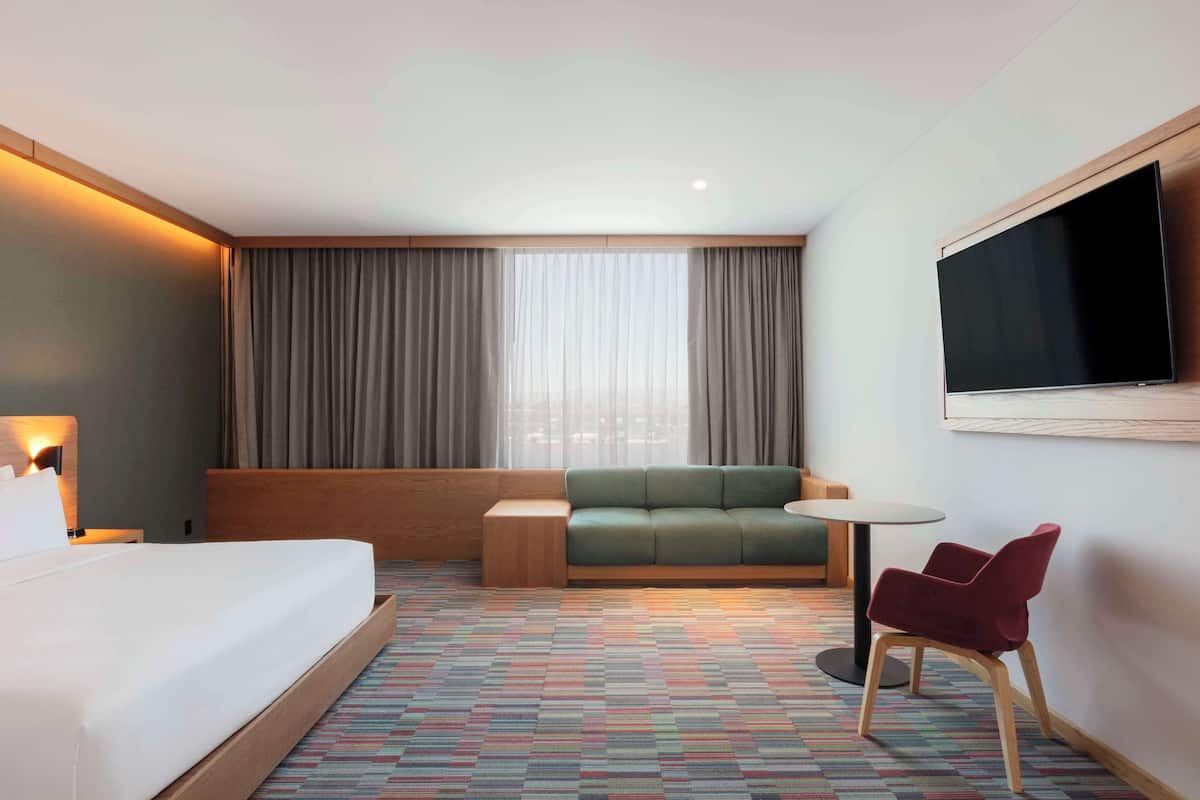 Une chambre d’hôtel avec un lit, un canapé, une petite table, une télévision et une moquette à motifs.