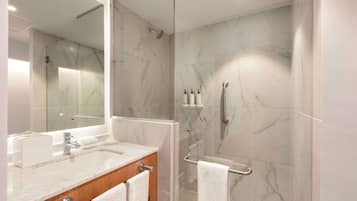 Un baño moderno con ducha revestida de mármol, zona de ducha con cerramiento de vidrio, tocador con lavabo y un espejo grande.