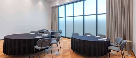Un salón de conferencias con dos mesas redondas, sillas grises y un ventanal con cortinas.