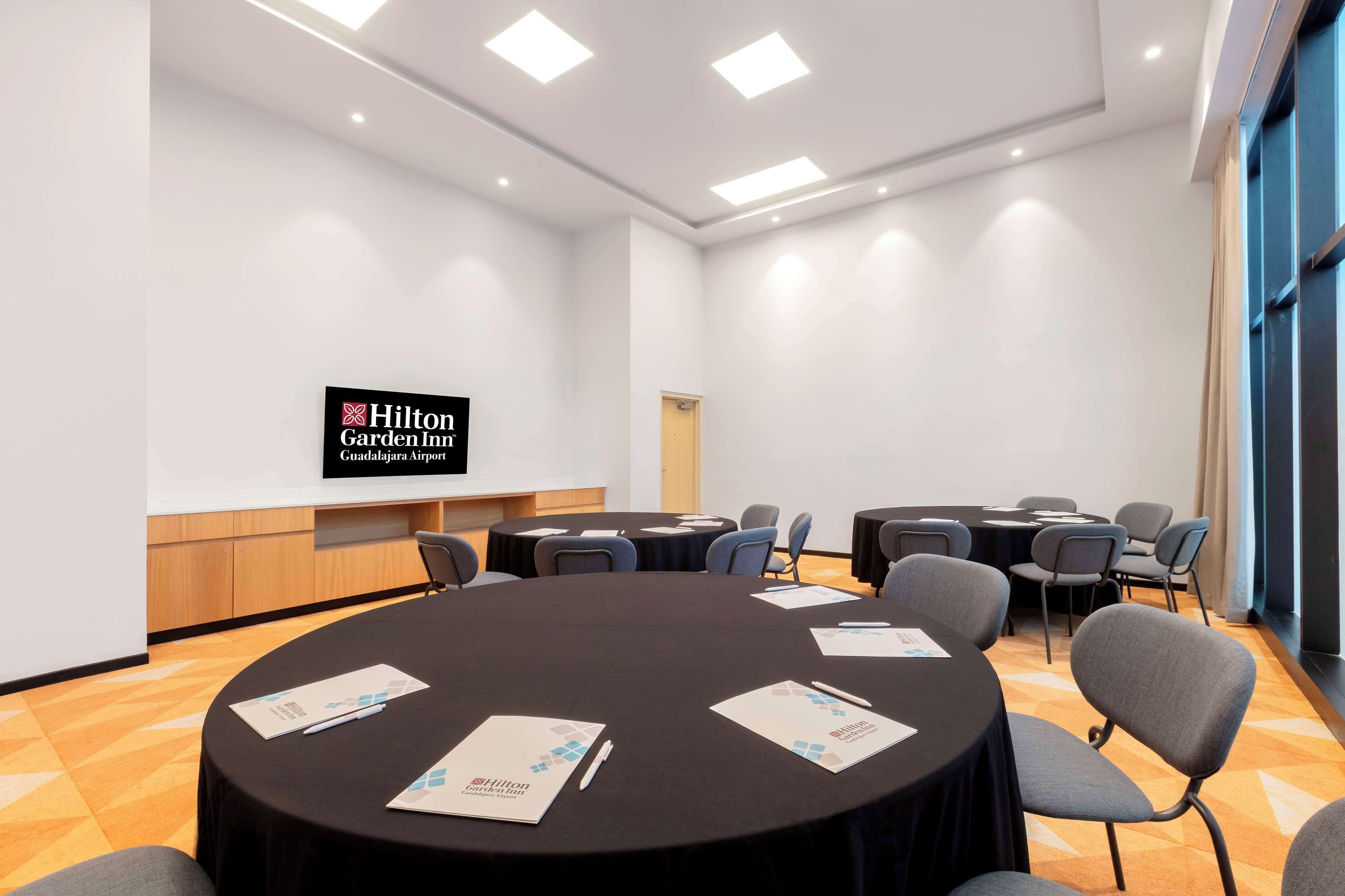 Una sala de conferències amb una taula rodona, cadires i una pantalla de presentació que mostra el logotip de Hilton Garden Inn.