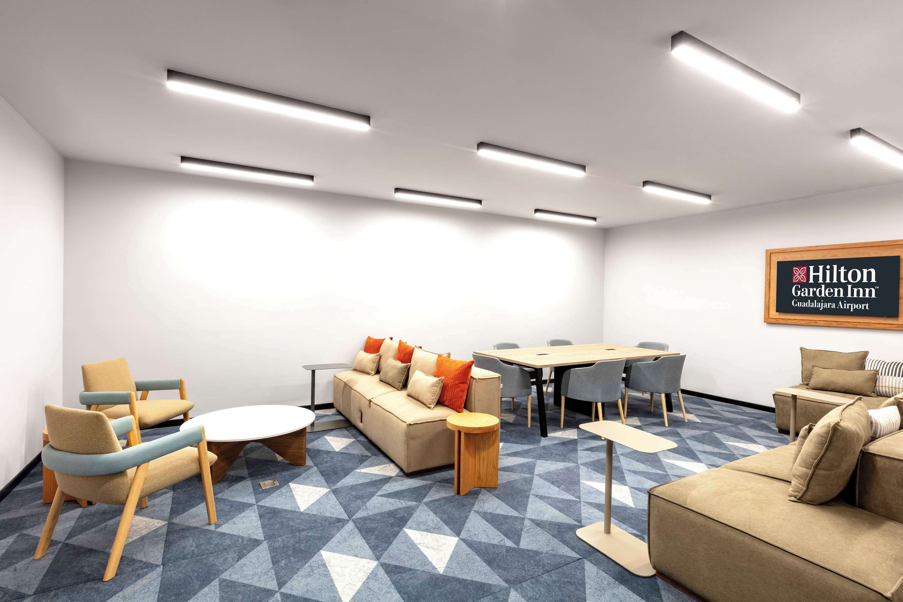 A modern hotel lobby with a sofa, chairs, a round table, and a carpeted floor.