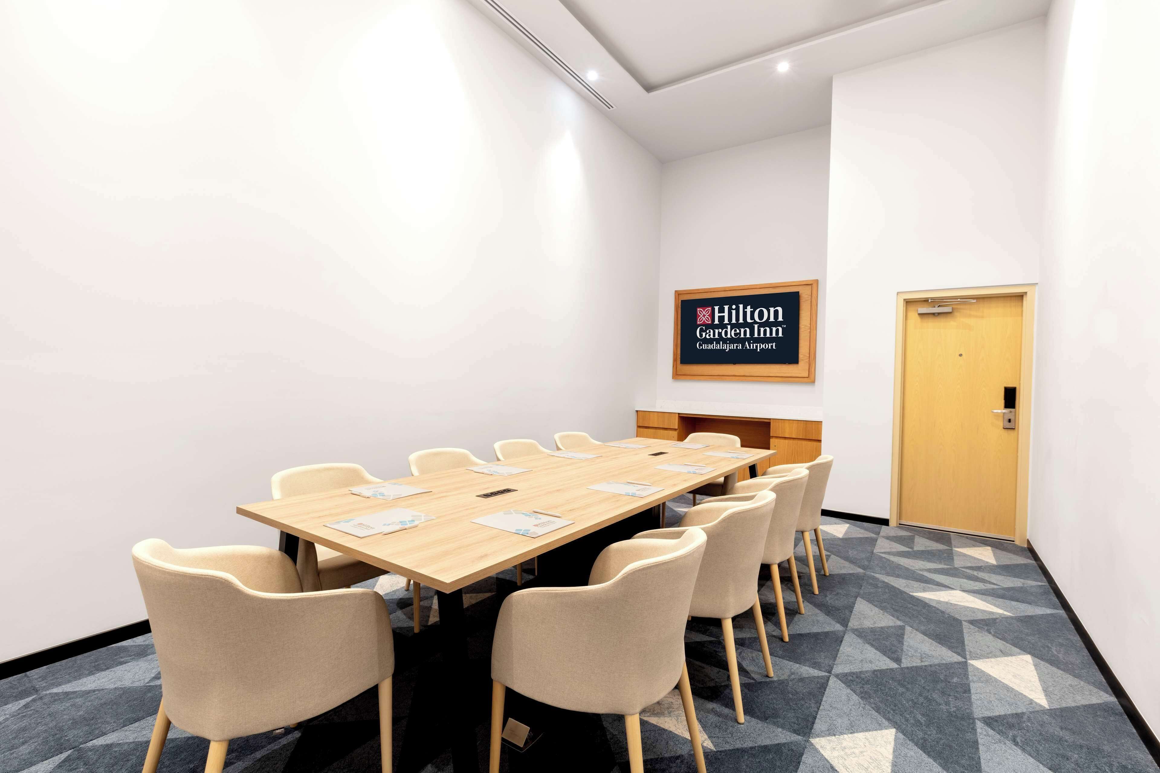 A conference room with a long table, beige chairs, a framed sign, and a carpeted floor.