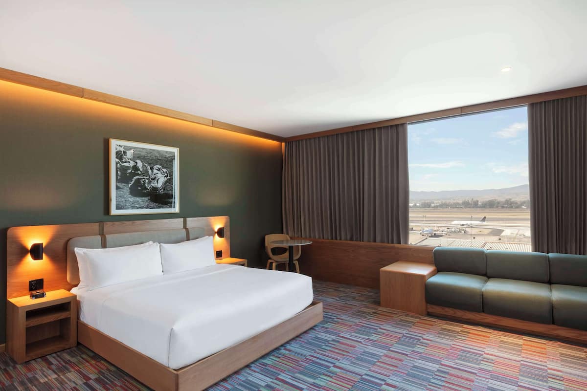 Une chambre d’hôtel avec un grand lit, un bureau, un canapé et une vue sur un aéroport.