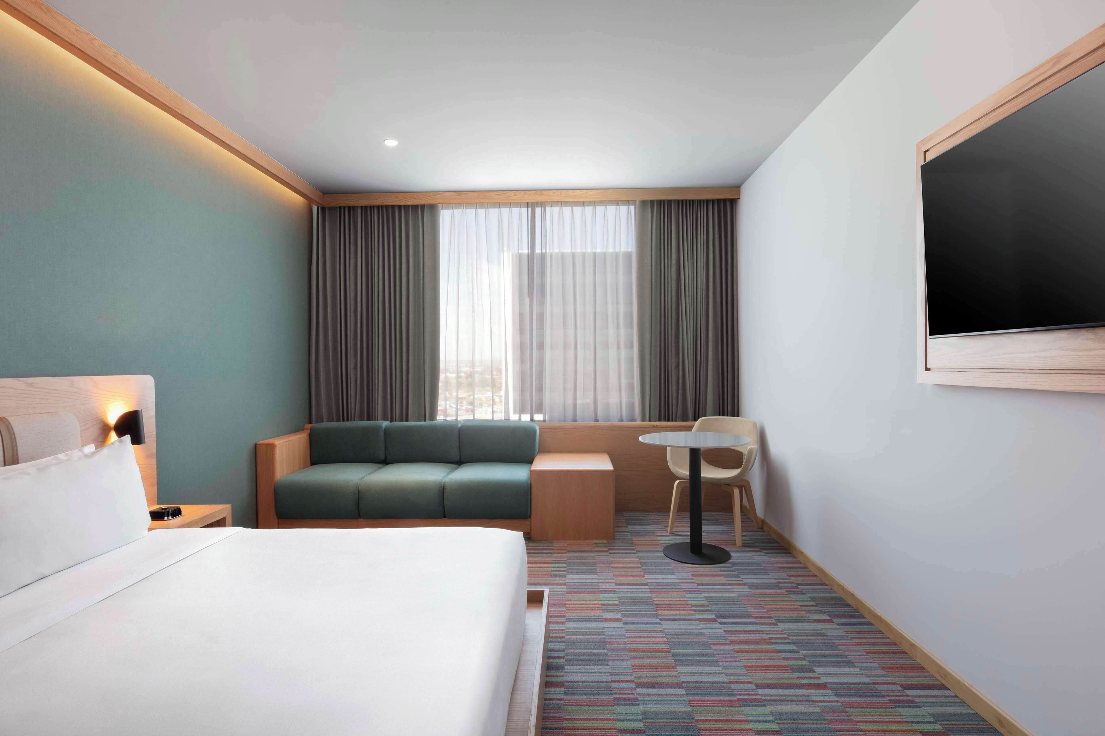 A hotel room with a bed, a green sofa, a small table, and a TV mounted on the wall.
