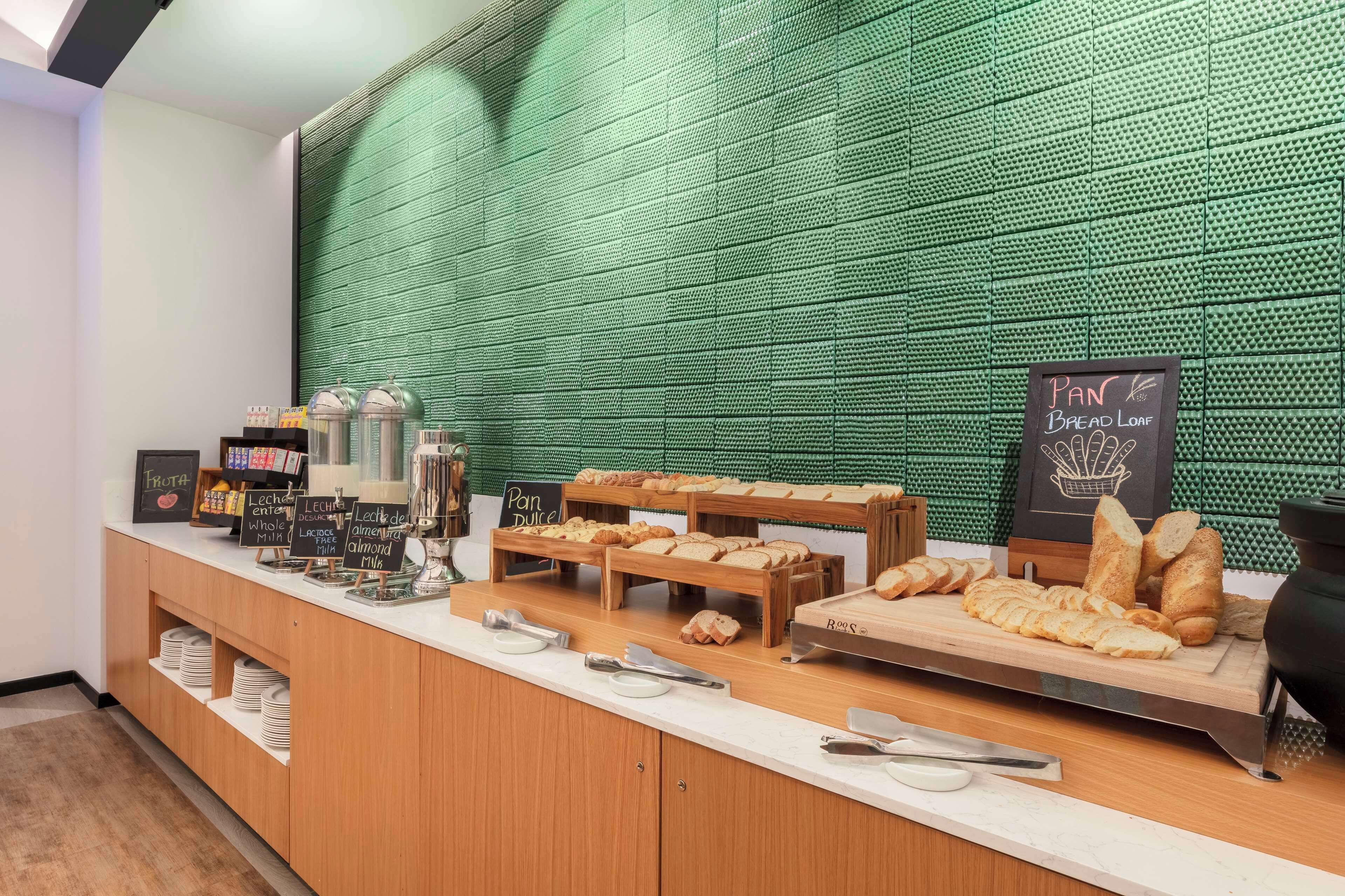 Un comptoir de boulangerie où sont exposés divers pains et pâtisseries, un tableau noir servant de menu et un mur vert à texture.