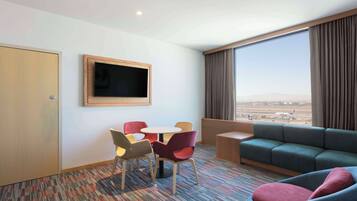 Una habitación de hotel con un ventanal grande, un televisor, un sofá y una pequeña mesa con sillas.