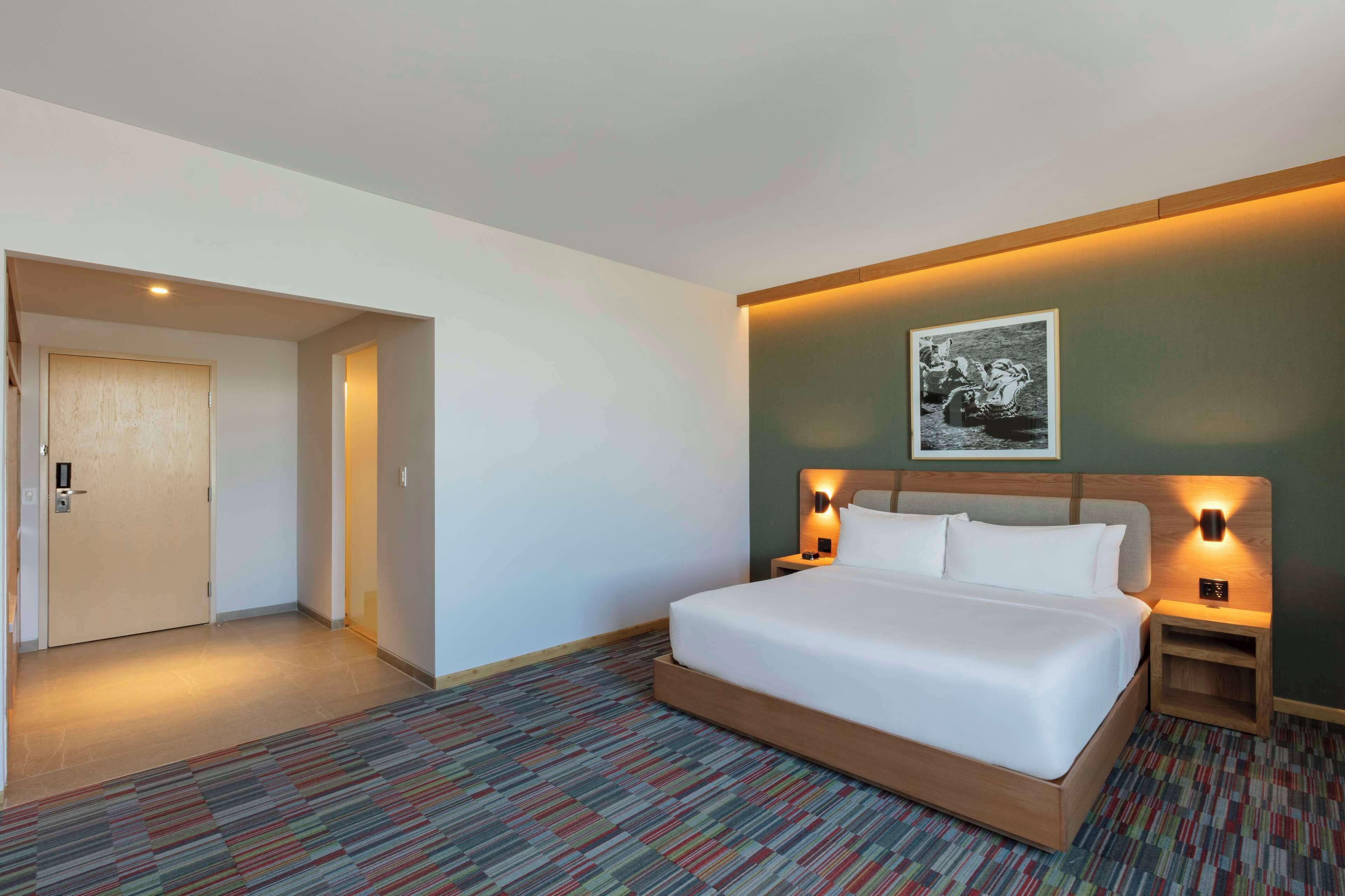 A hotel room with a large bed, two bedside tables with lamps, a framed picture on the wall, and a carpeted floor.