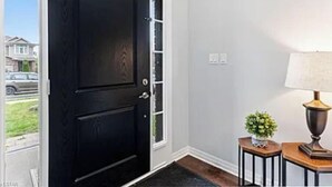A black door with a glass panel, a white wall with a light switch, and a small table with a lamp and a plant. - Pookah Bill House! (London)
