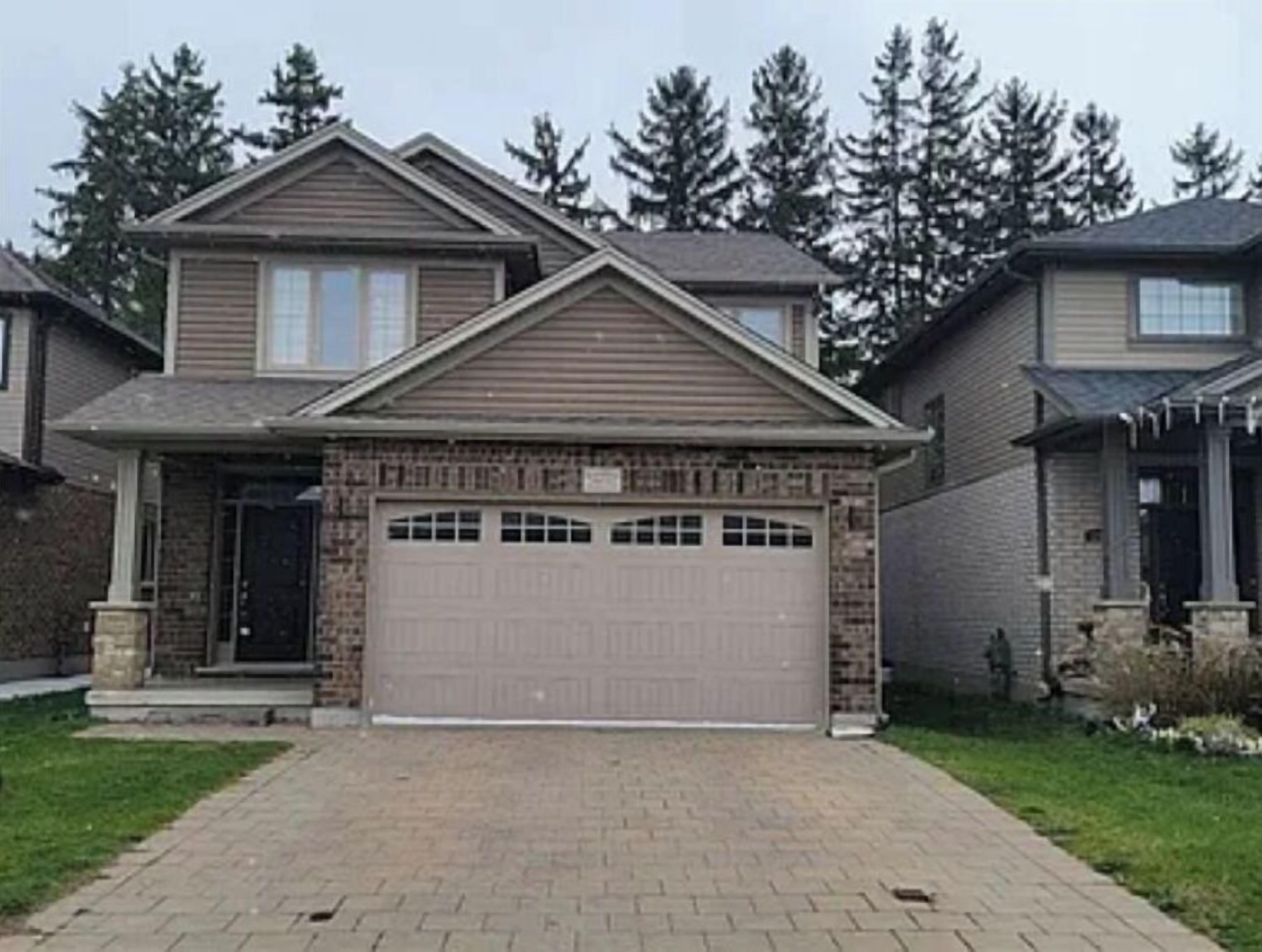 Une maison à deux étages avec un garage, une façade en briques et une allée menant à l’entrée.