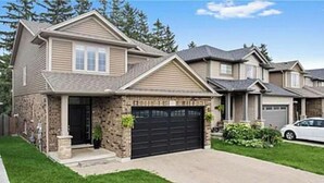 A two-story house with a stone facade, a black garage door, and a well-maintained lawn. - Pookah Bill House! (London)
