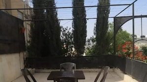 Een dakterras met een tafel en vier stoelen, omgeven door een metalen hek en bomen.