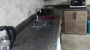 Een keuken met granieten aanrecht, houten kastjes, een magnetron, een waterkoker en een spoelbak.