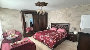 Een slaapkamer met een groot bed, een zithoek met een fauteuil, een dressoir en een spiegel.