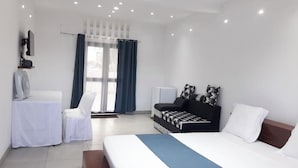 A modern hotel room with a large bed, a sofa, a chair, a desk with a fan, and a TV on the wall. - Espace le Majestic Toamasina (Toamasina)