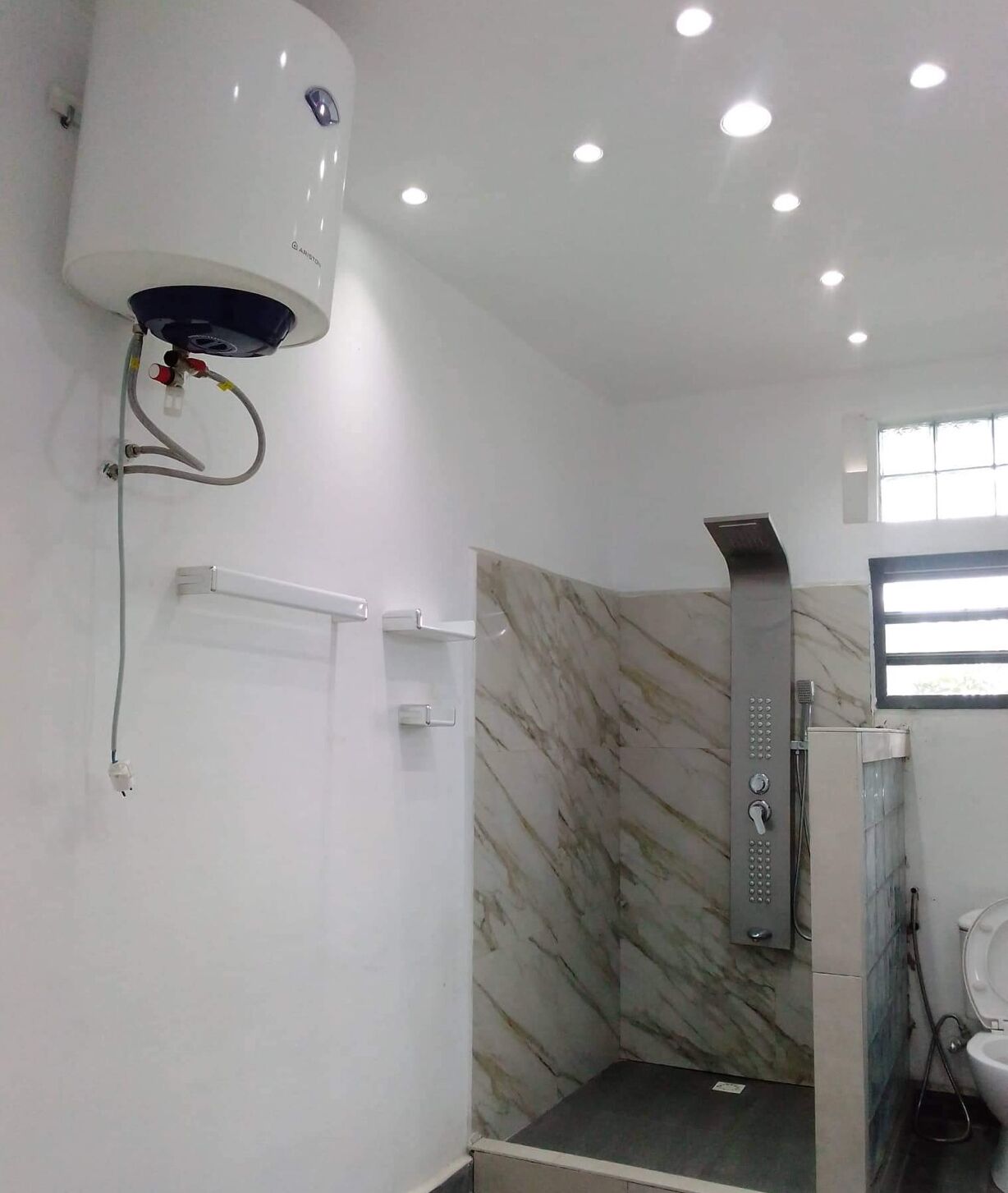 A modern bathroom with a shower, marble tiles, a water heater, and a window.