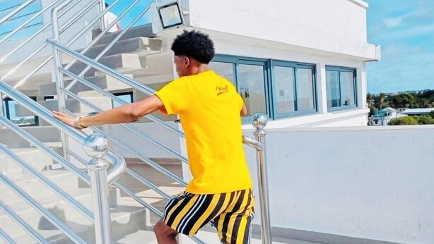 A person descending a staircase with metal railings, wearing a yellow shirt and striped shorts. - Espace le Majestic Toamasina (Toamasina)