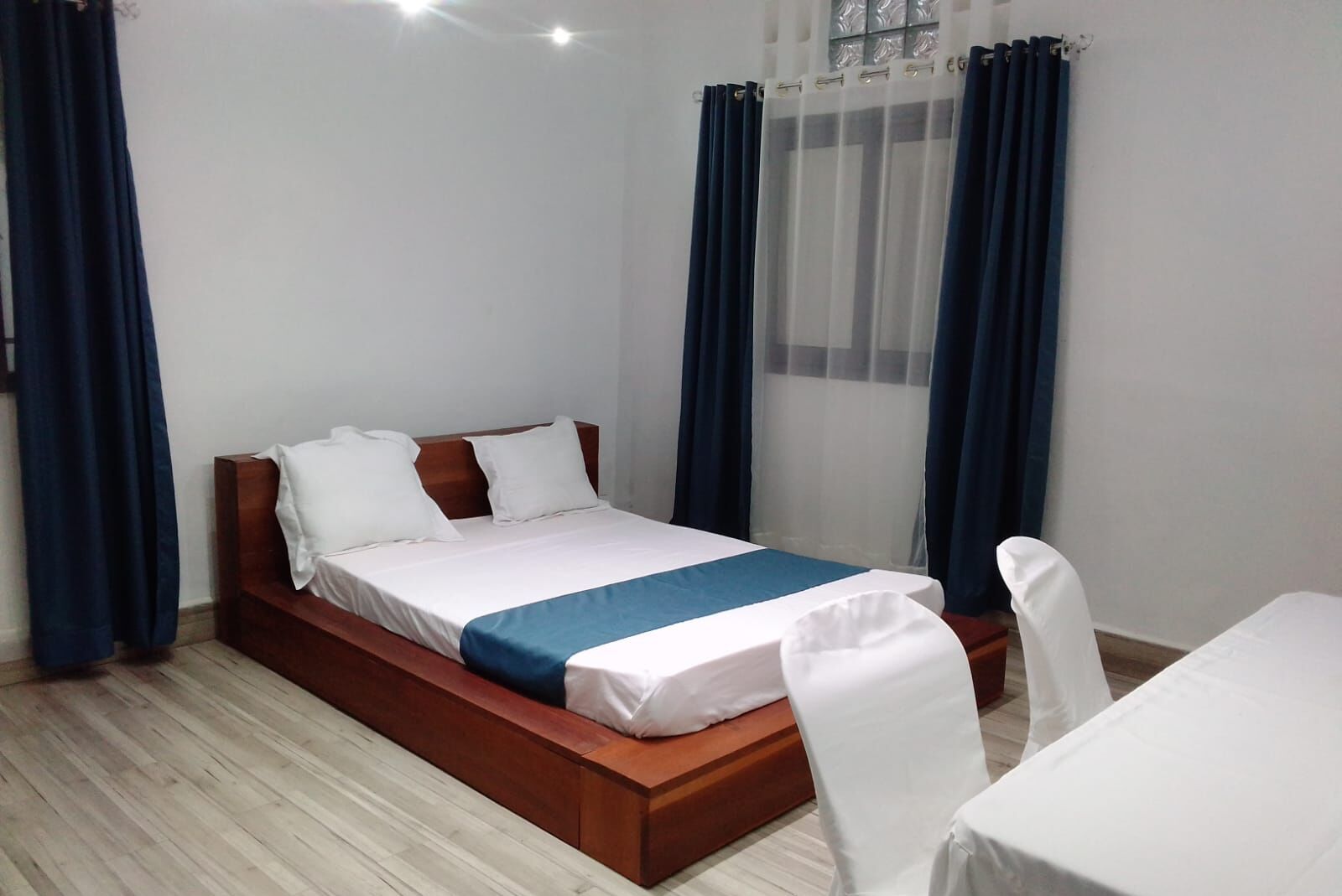 A neatly arranged bedroom with a wooden bed, white bedding, and a blue accent.