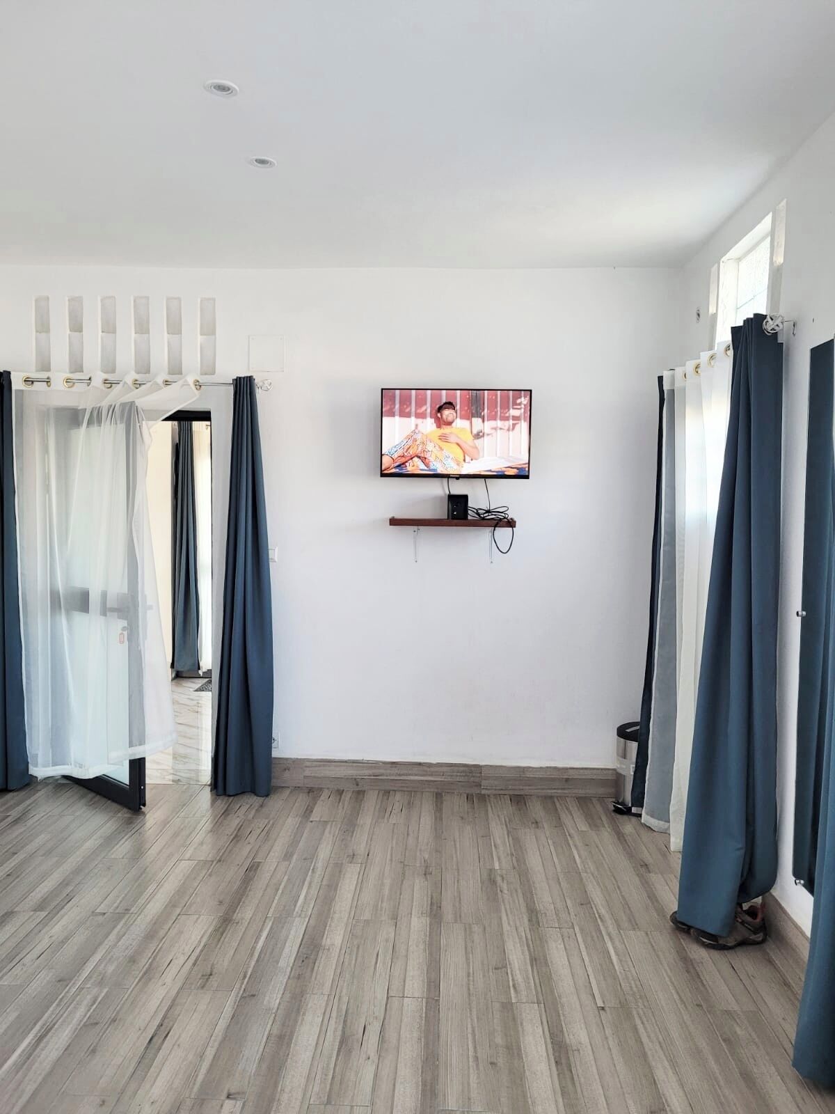 A room with a wooden floor, a mounted TV, and a window with curtains.