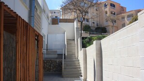 A narrow alleyway with a wooden pergola on one side and a concrete wall on the other. A set of stairs leads up to a building with a stone facade and a balcony. - Apartment right on the beachfront! - Beach - SweetHomeRooms (Cabo de Palos)