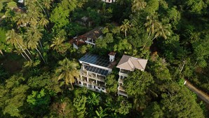 An aerial view of a multi-story building with solar panels on the roof, surrounded by dense tropical vegetation. - LARA'S PLACE - THE APARTMENT (Unawatuna)