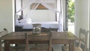 A room with a wooden dining table, four chairs, a bed with a canopy, and a ceiling fan. - LARA'S PLACE - THE APARTMENT (Unawatuna)