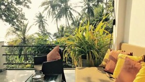A balcony with a glass table, a sofa with cushions, and a large potted plant. - LARA'S PLACE - THE APARTMENT (Unawatuna)