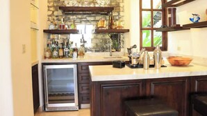A kitchen with a stone backsplash, wooden cabinets, a built-in oven, and a large island with bar tools. - Villa de Lujo Buena Vista 3 (Cabo San Lucas)
