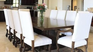 A dining area with a large oval table surrounded by white upholstered chairs, a vase with flowers, and pendant lighting. - Villa de Lujo Buena Vista 3 (Cabo San Lucas)