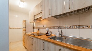 A kitchen with wooden cabinets, a stainless steel sink, and a tiled backsplash. - AlmeriaSuite Beach&Sun (Almería)