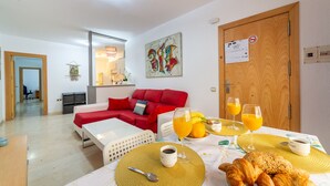 A modern living room with a red sofa, a dining table set with breakfast, and a kitchen in the background. - AlmeriaSuite Beach&Sun (Almería)
