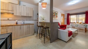 A modern kitchen with wooden cabinets, a central island, and a dining area with a red sofa and white table. - AlmeriaSuite Beach&Sun (Almería)