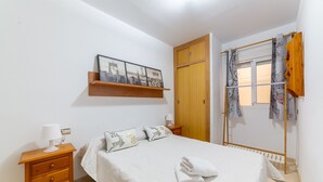 A bedroom with a bed, a nightstand, a wooden dresser, a door, and a window with curtains. - AlmeriaSuite Beach&Sun (Almería)