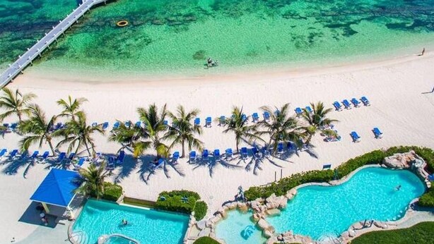 An aerial view of a beach resort with a swimming pool, palm trees, and a pier. - Sea Glass at the Reef - Luxury King Beach Front Condo On The Beach (Colliers Bay)