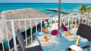 A beachside restaurant with thatched umbrellas, dining tables, and chairs, overlooking the ocean. - Sea Glass at the Reef - Luxury King Beach Front Condo On The Beach (Colliers Bay)