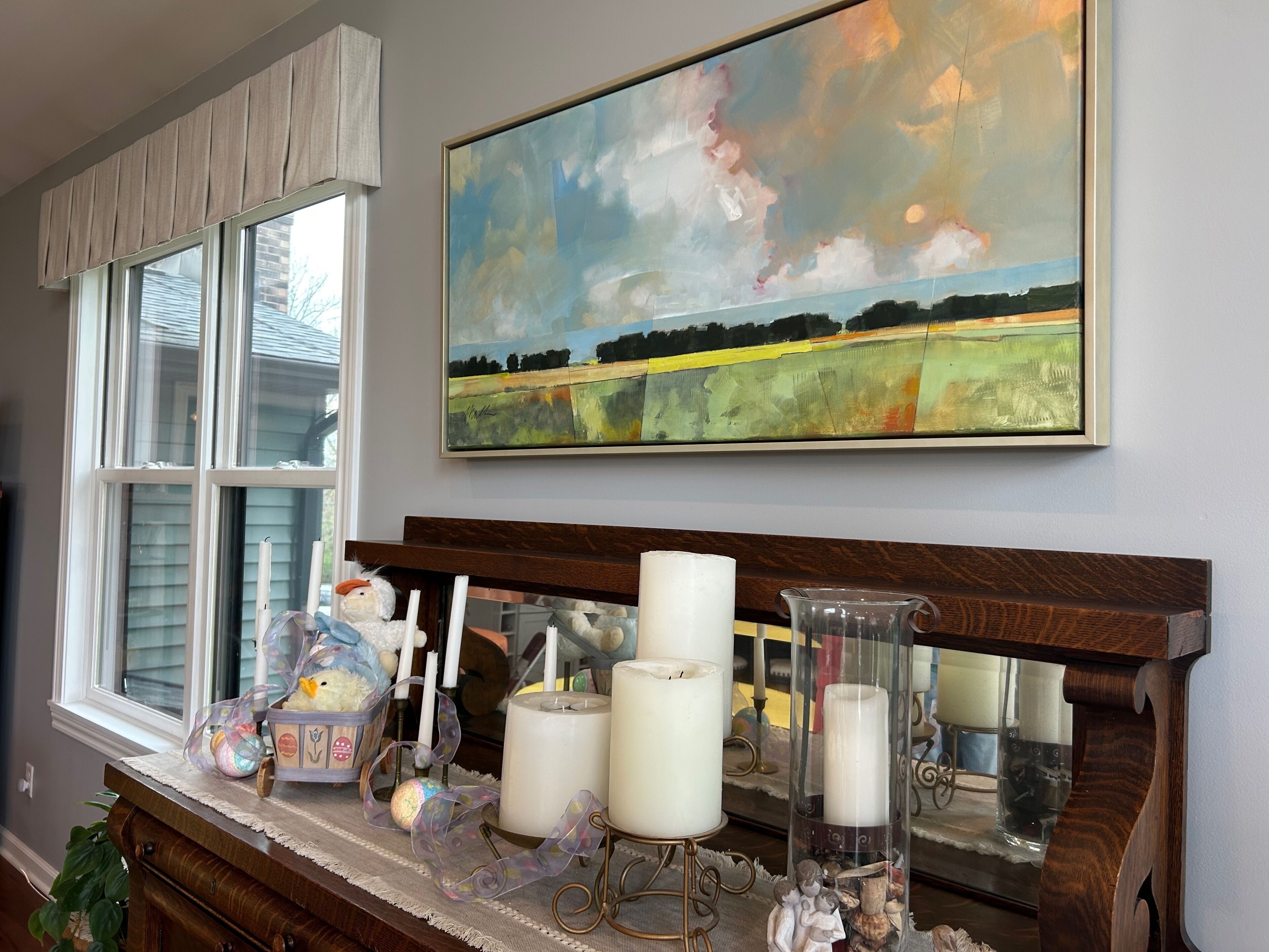A room with a window, a painting, and a table with candles and decorative items.