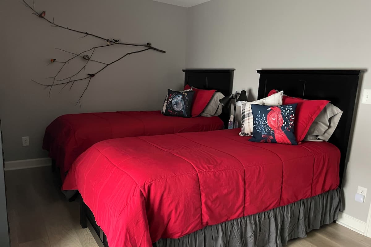 Een slaapkamer met twee bedden, elk met een zwart hoofdeinde en rode beddengoed.