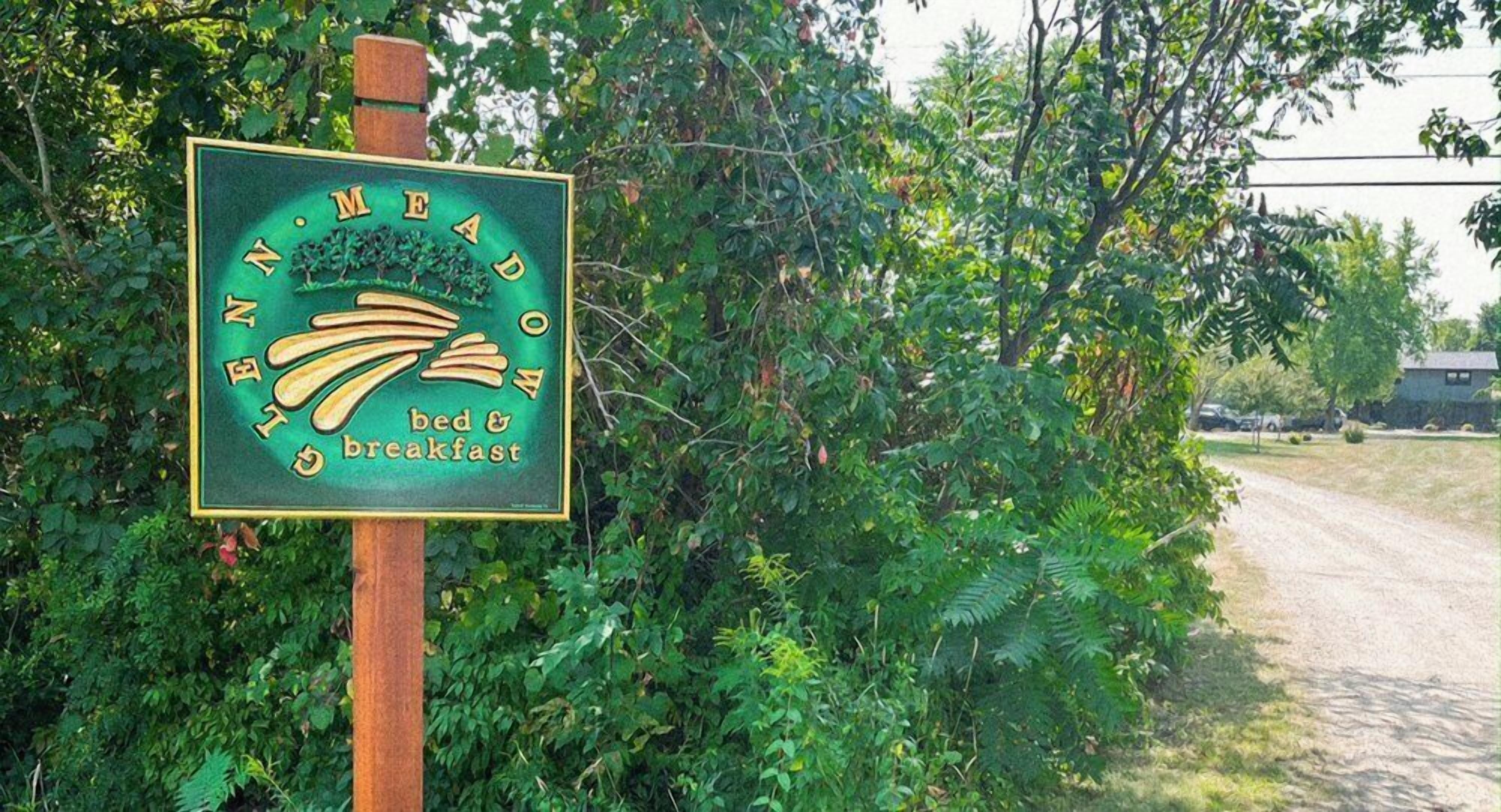 A sign for a bed and breakfast named "N.M. Meadow" with a rustic wooden post and lush greenery in the background.