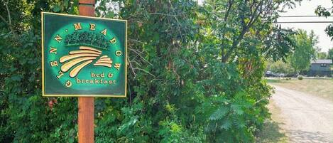 A sign for a bed and breakfast named "N.M. Meadow" with a rustic wooden post and lush greenery in the background.