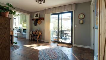 A spacious living room with a large sliding glass door leading to a patio, a kitchen in the background, and a wooden floor.