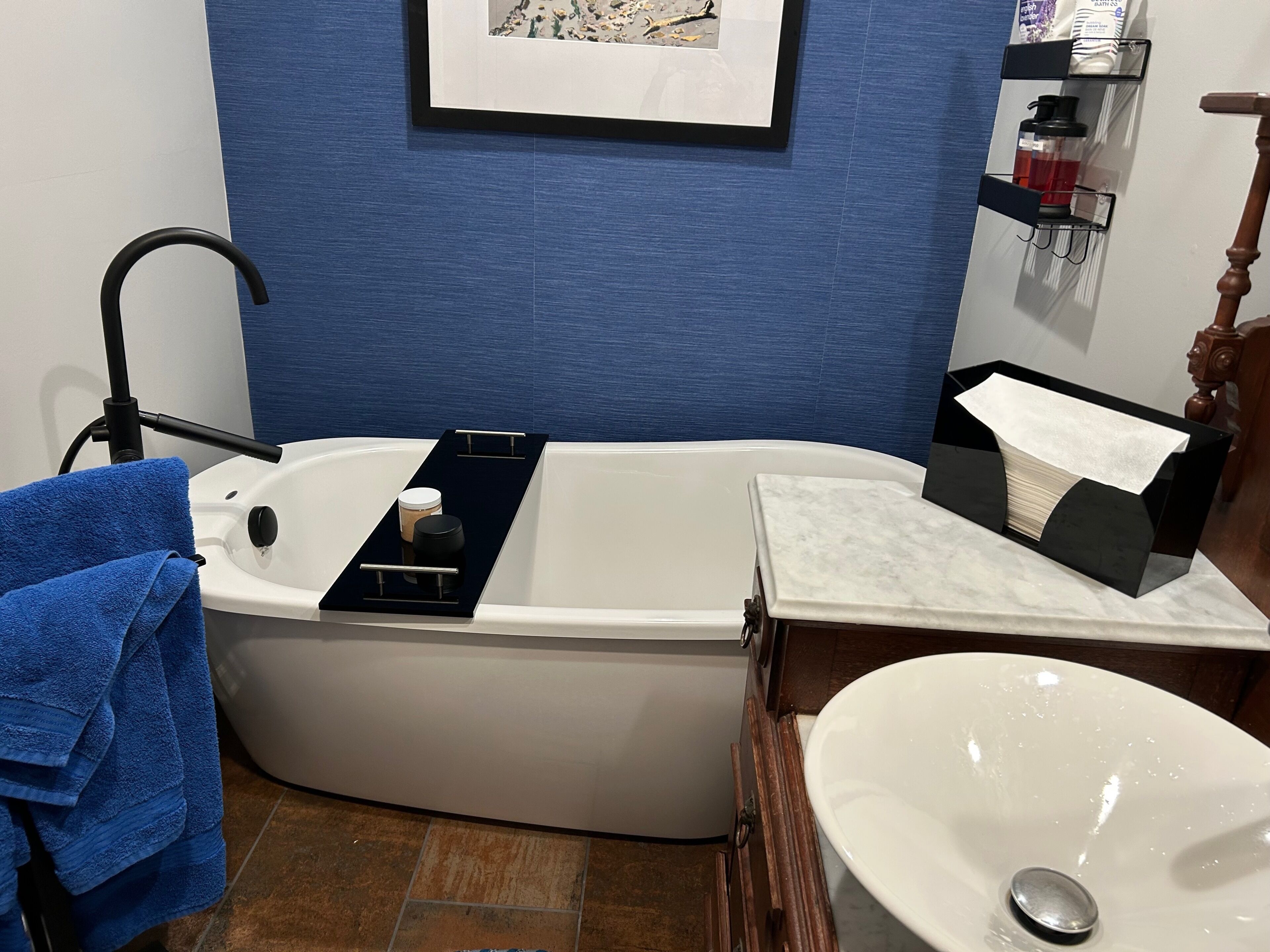 Un baño con bañera, lavamanos, toallero y estante con artículos de aseo.