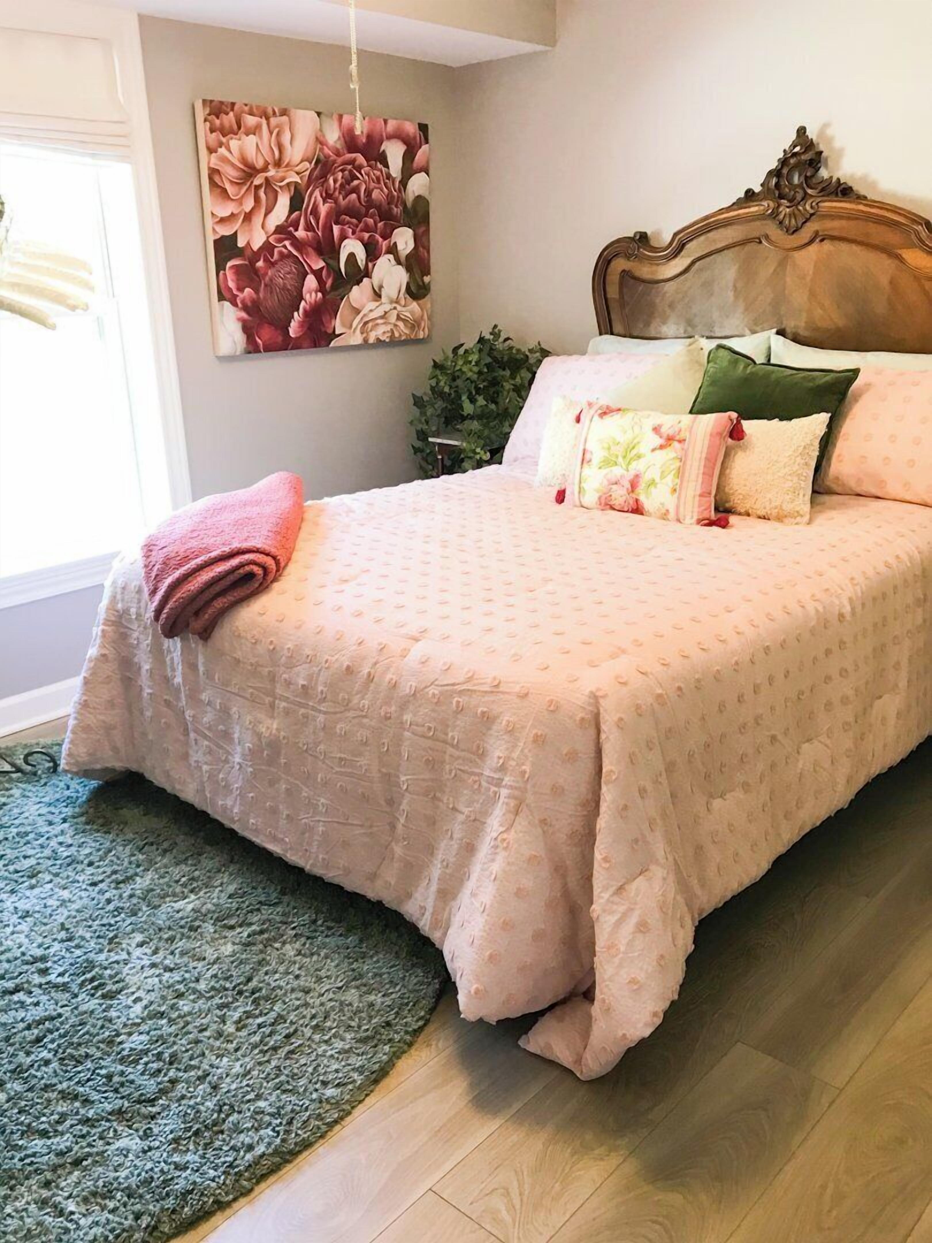 Ein Schlafzimmer mit einem großen Bett, einem grünen Teppich, einem hölzernen Kopfteil und einem floralen Wandbild.