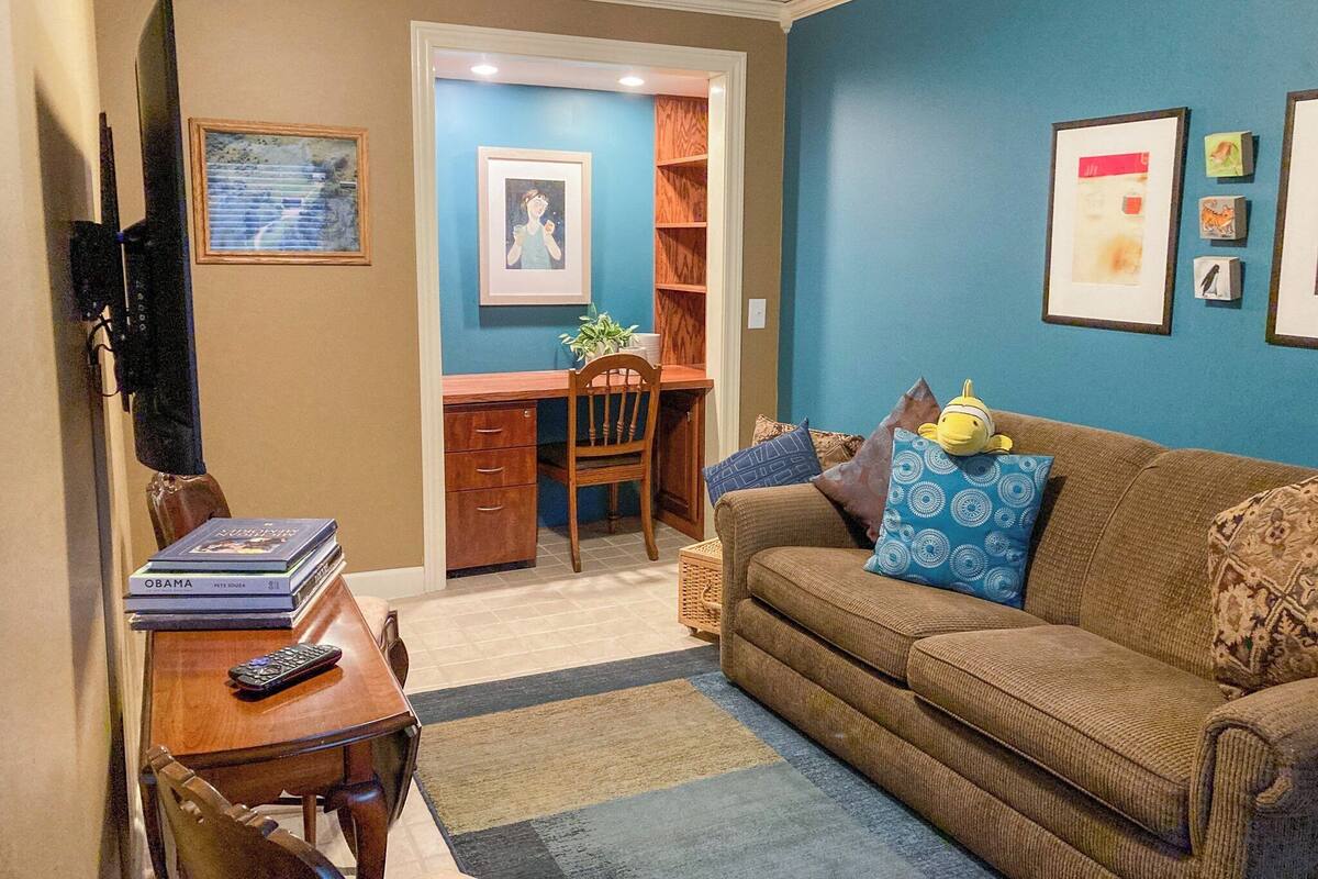 Een woonkamer met een bruine bank, een houten salontafel en een televisie links. Er is een boekenkast met boeken en een ingelijst beeld aan de muur.