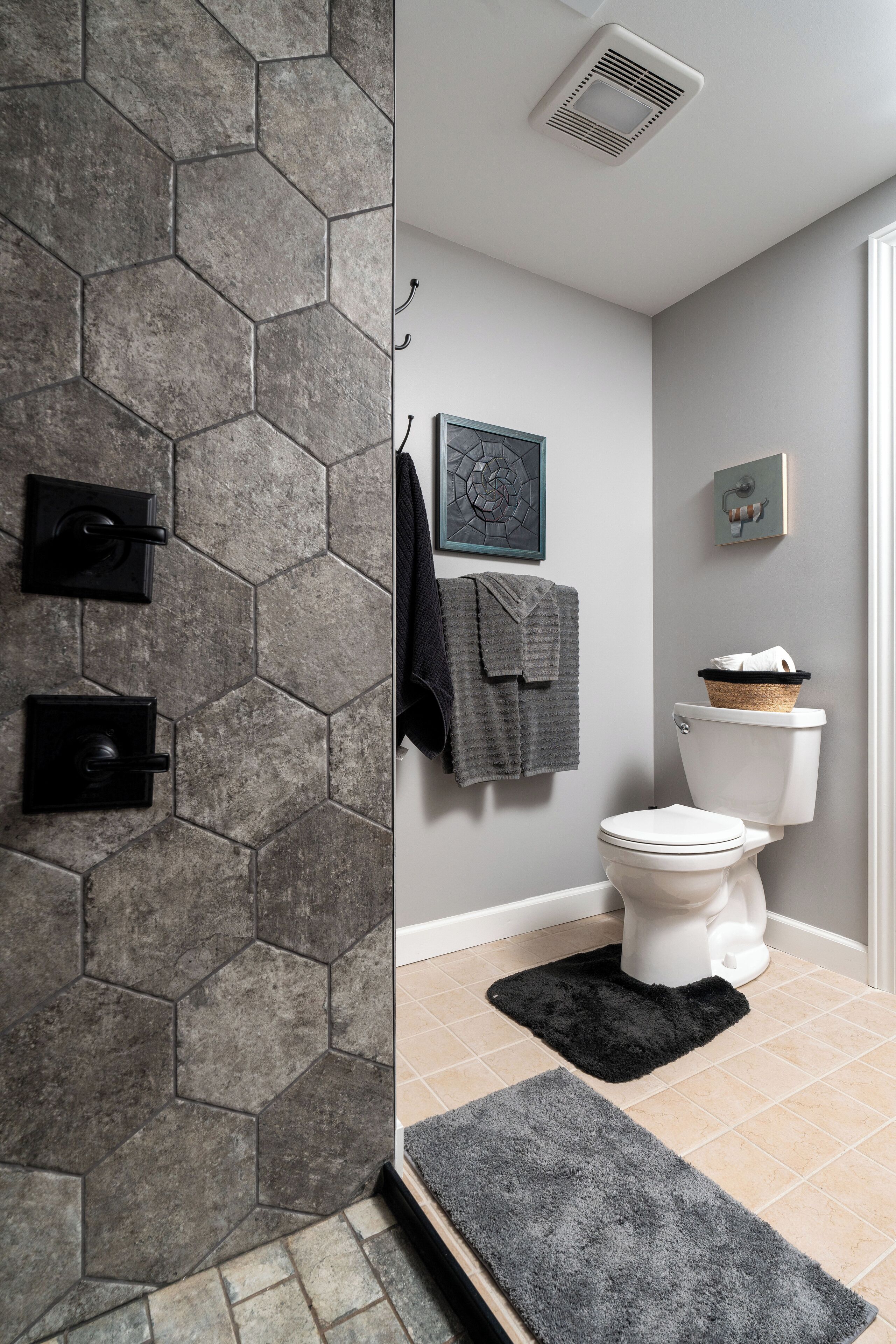 A bathroom with hexagonal stone walls, a white toilet, a black rug, and a towel rack with towels.