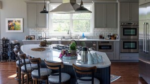 Une cuisine moderne dotée d’un grand îlot central, d’appareils électroménagers en acier inoxydable et offrant une vue sur l’extérieur grâce à une grande fenêtre.