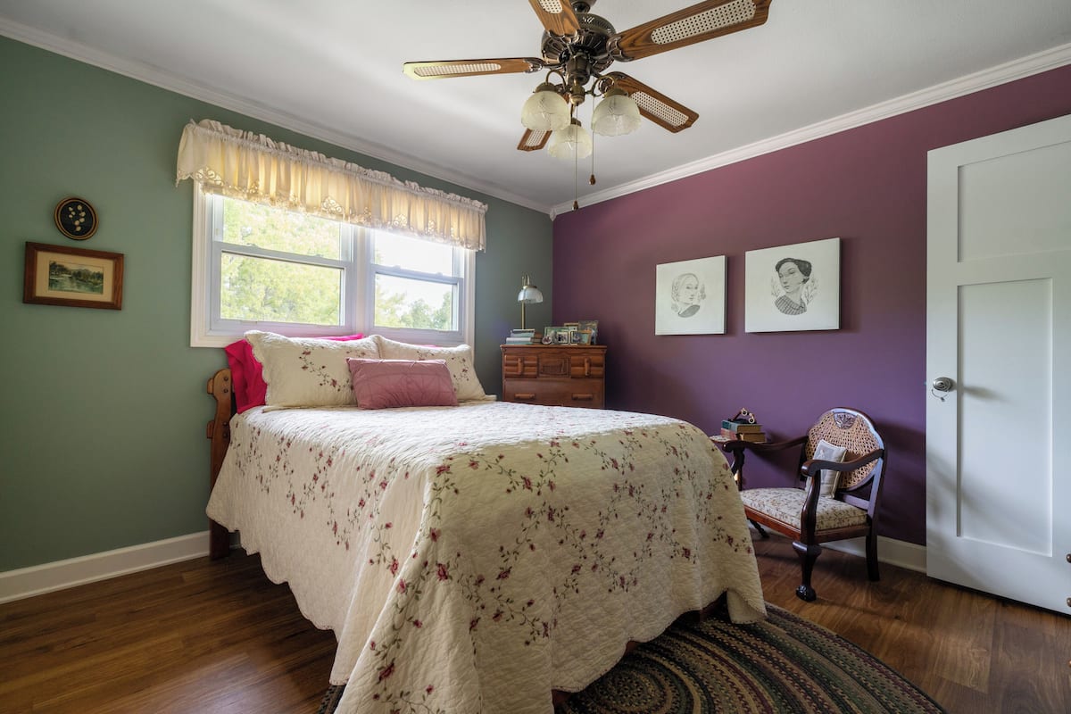 Een slaapkamer met een bed, een dressoir, een stoel, een plafondventilator en een raam.
