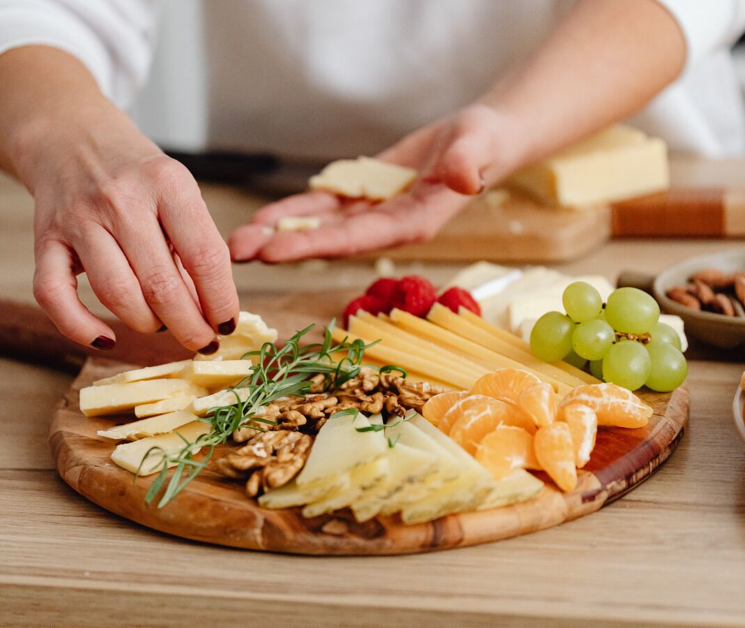 A wooden board with various cheeses, fruits, and nuts.