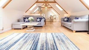 Un loft spacieux avec de hauts plafonds, des poutres apparentes, un coin repas et un espace salon avec des canapés et une table basse.