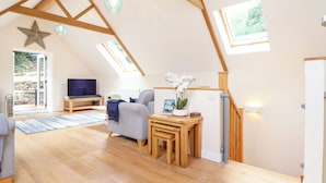 Un loft spacieux avec de hauts plafonds, des poutres apparentes, une grande fenêtre et un coin salon confortable avec un canapé et une petite table.